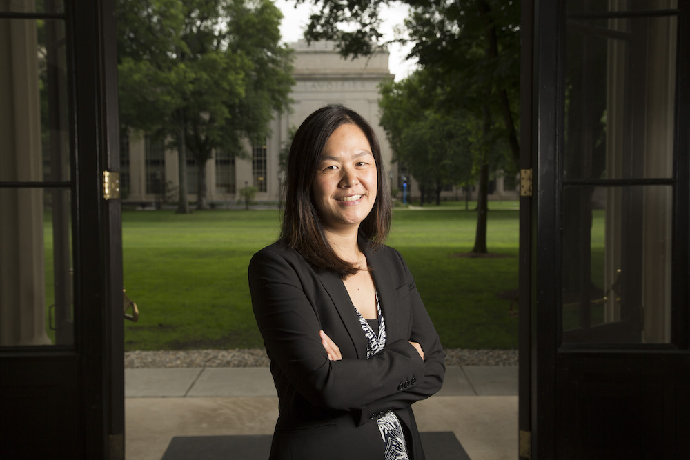 Evelyn Wang standing with her arms folded in front of MIT's Killian Court