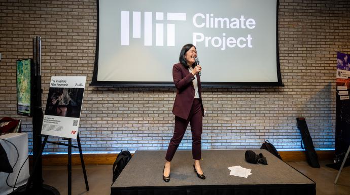 Evelyn Wang standing on a small dais with a microphone in her hand; behind her on a screen is the MIT Climate Project logo